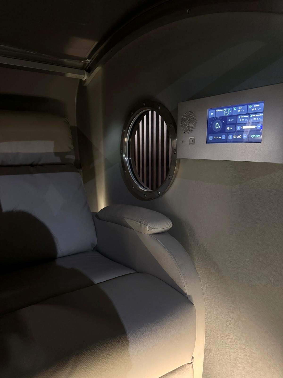 Inside the hyperbaric chamber at Vytara, with a cushioned recliner, porthole window, and the session controls within easy reach