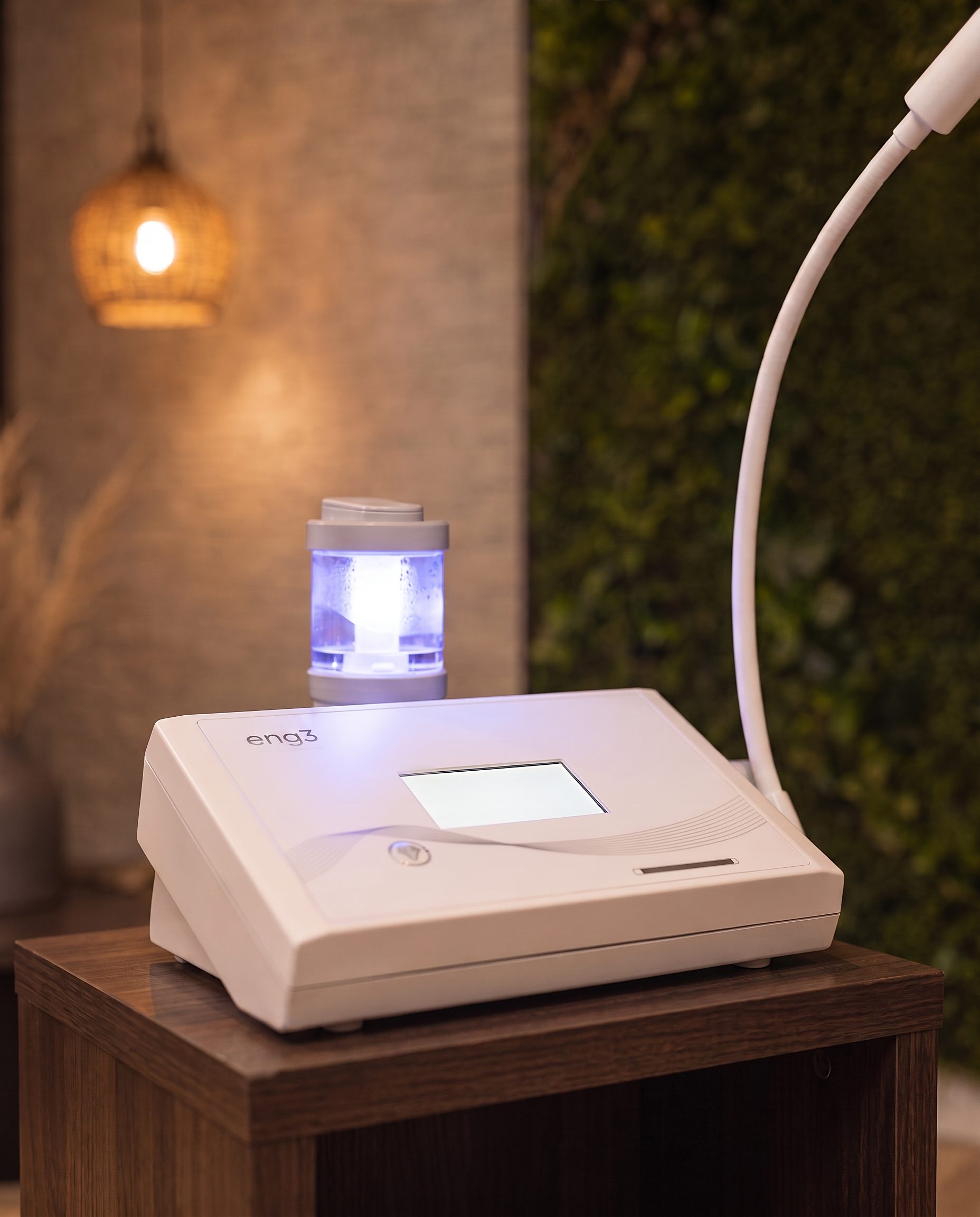 The NanoVi device on its side table at Vytara: the glowing humidifier chamber and flexible delivery arm, with the living moss wall behind